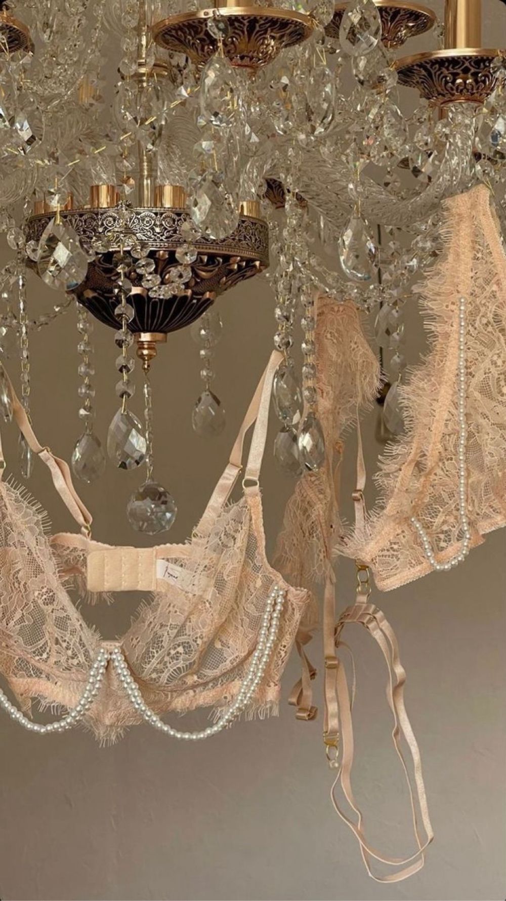 Blush lace lingerie and strands of pearls draped over a crystal chandelier