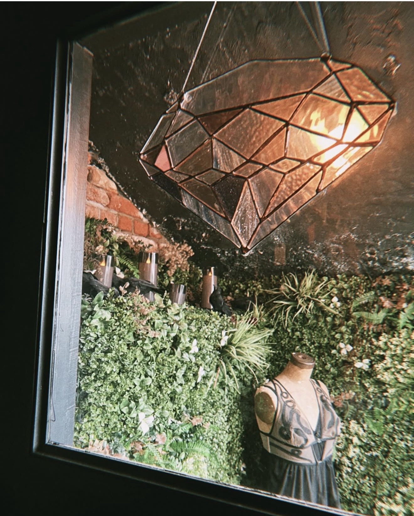 Stained-glass diamond above a living plant wall and dress form inside Hidden Gem Hudson